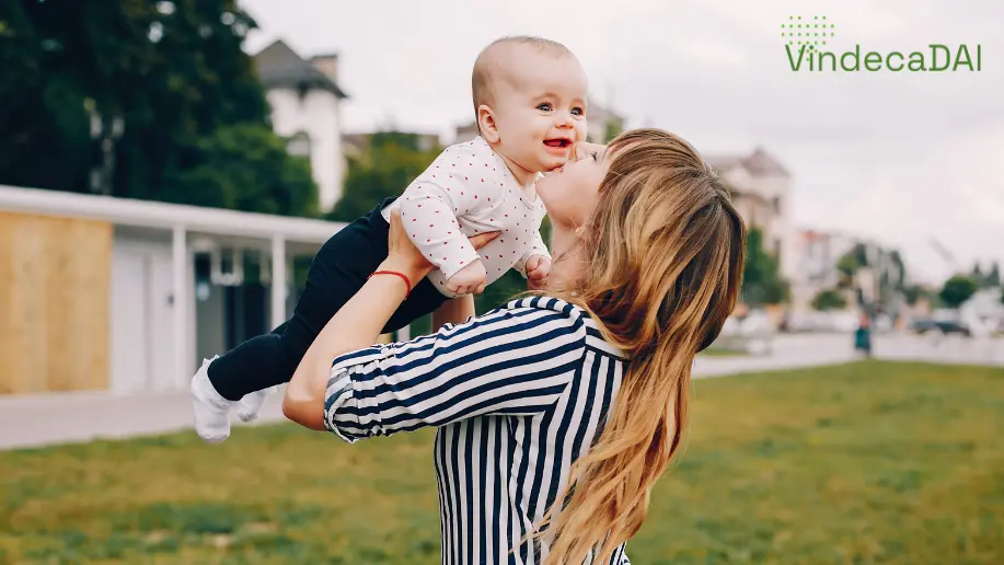 mama-cu-bebeluș-în-brațe-când-îl-sărută-și-se-joacă-în-curte-și-cu-fundal-de-iarbă-în-spate